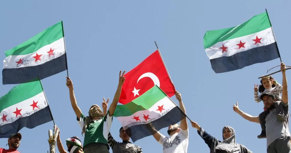 PIDEN PAZ. Refugiados sirios agitan banderas independentistas y turcas, en un campamento fronterizo, en la provincia de Hatay, en Turquía. REUTERS