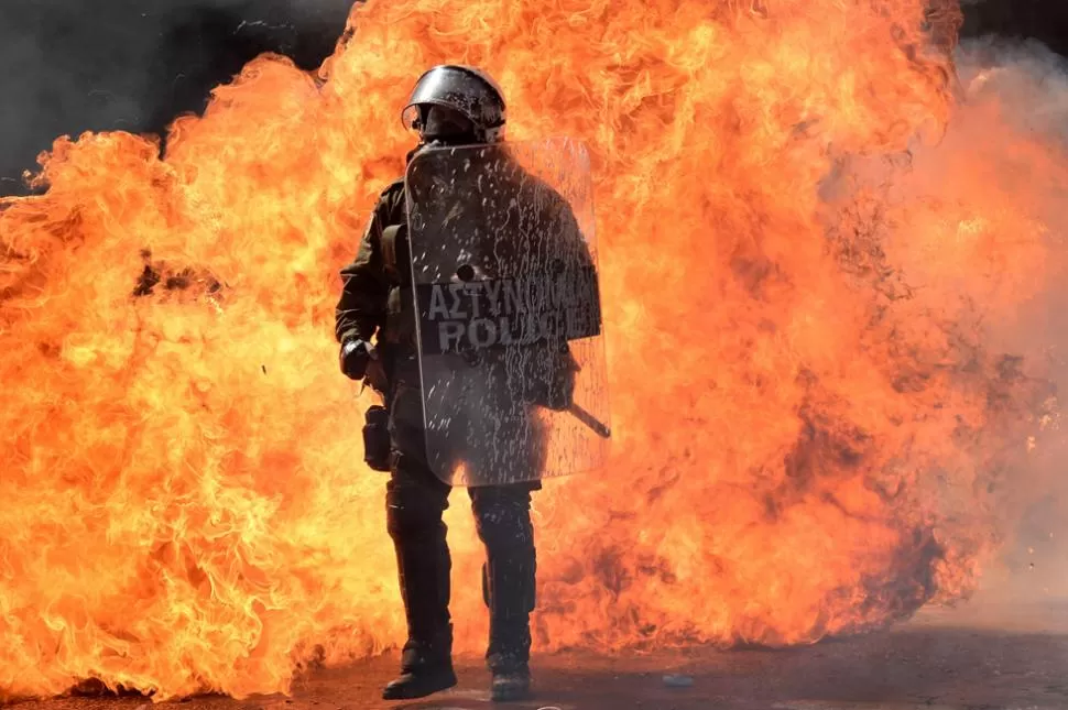 GRECIA ESTÁ QUE ARDE. Un policía contraste con el fuego que se inició en la protesta. AFP.