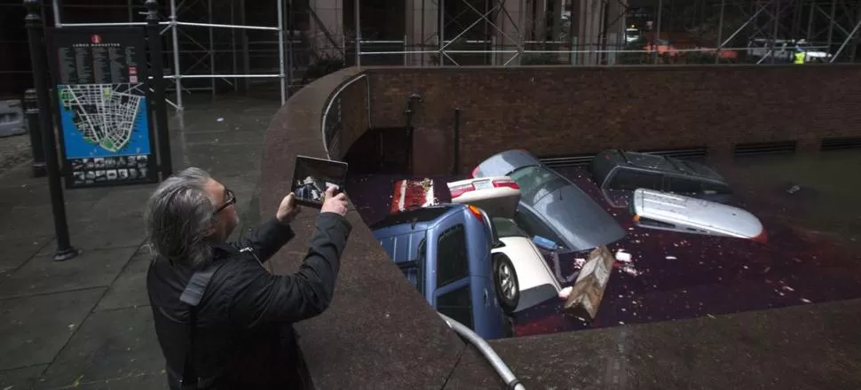 EN MANHATTAN. Con un iPad, un neoyorquino fotografía a una pila de vehículos sumergidos en una calle del distrito financiero de Nueva York. FOTOS REUTERS