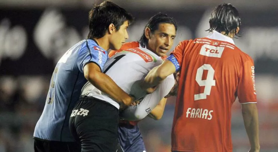AGRESION. Jugadores de Independiente y Belgrano ayudan al arquero Olave a alejarse de las bombas de estruendo que caían sobre su arco, en el partido que fue suspendido y que continuará mañana con los 45 minutos restantes. 