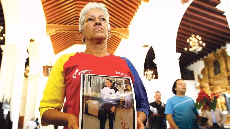 REZOS. Una venezolana asiste a misa con una foto de Chávez en Caracas. REUTERS.