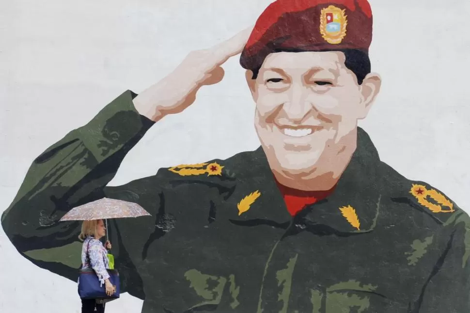 EN CARACAS. Un grafitti del presidente-comandante sobresale en una pared, ante el paso de una venezolana. AFP (ARCHIVO)