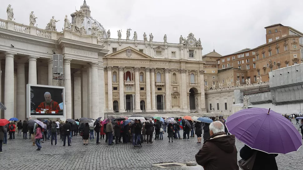 AUDIOVISUAL. Fieles siguen la misa Pro eligendo Pontifice a través de una de las pantallas instaladas en la Plaza de San Pedro del Vaticano. EFE