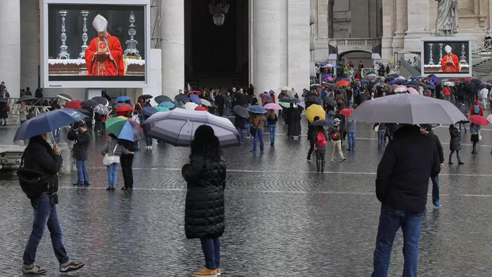 BAJO LA LLUVIA. Fieles siguen la misa a través de las pantallas instaladas en la Plaza de San Pedro, del Vaticano. EFE
