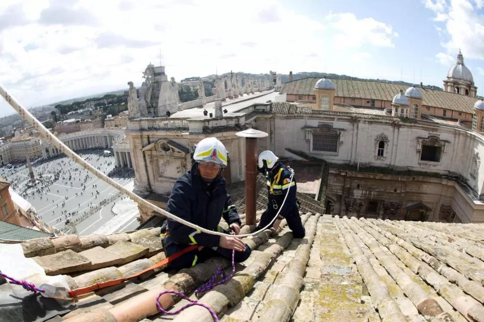 TRABAJOS. Dos bomberos colocan la chimenea en los techos de la Capilla Sixtina, por donde saldrá la fumata que anunciará al nuevo sumo pontífice. EFE