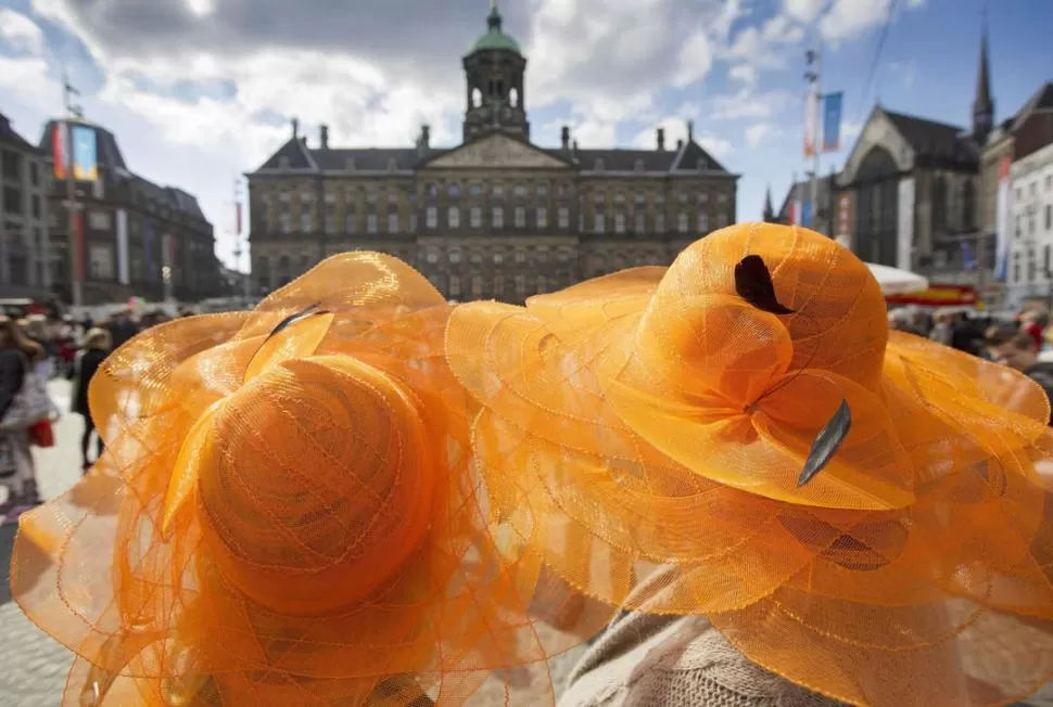 PREPARADOS. En la plaza Dam de Amsterdam, los turistas y los vecinos de la capital holandesa llevan prendas naranjas en honor al futuro rey. FOTOS EFE - REUTERS