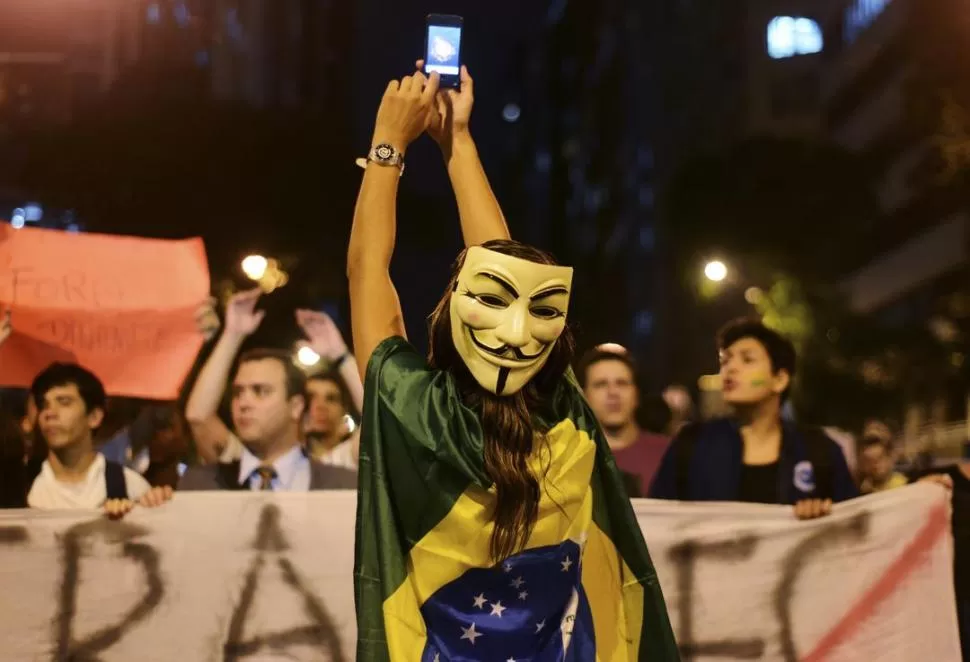 PROTESTAS. Una manifestante con la máscara de Guy Fawkes (luchador inglés del siglo XVI) saca fotos en Río. REUTERS