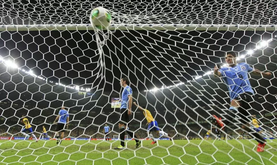 ENTRE EL FESTEJO Y LA BRONCA. Paulinho marcó el gol de la victoria de Brasil a minutos del final y sus compañeros inician la celebración. Suárez, decepcionado, revienta el balón contra la red. Fue 2 a 1. REUTERS