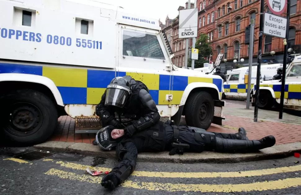 GOLPEADO. Un policía asiste a su colega durante los choques en Belfast.  REUTERS