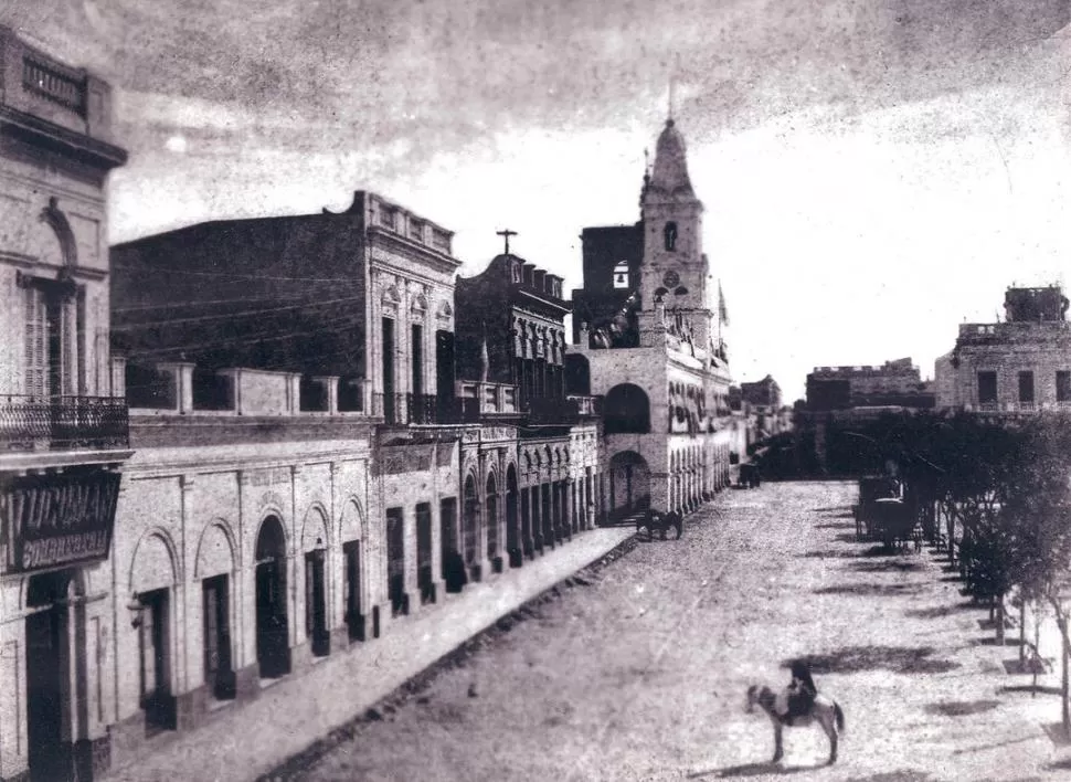 VEREDA DEL CABILDO. A fines del siglo XIX, se ve la calle 25 de Mayo, frente a la plaza. Sobre la izquierda, el edificio de una planta con cinco aberturas es la casa natal de Alberdi, con su frente ya modificado. 