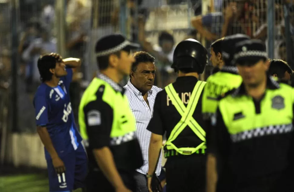 EL PEOR MOMENTO. Un grupo de policías protege al técnico Ricardo Rodríguez mientras César Montiglio se toma la cabeza al observar lo que ocurría en las tribunas. 