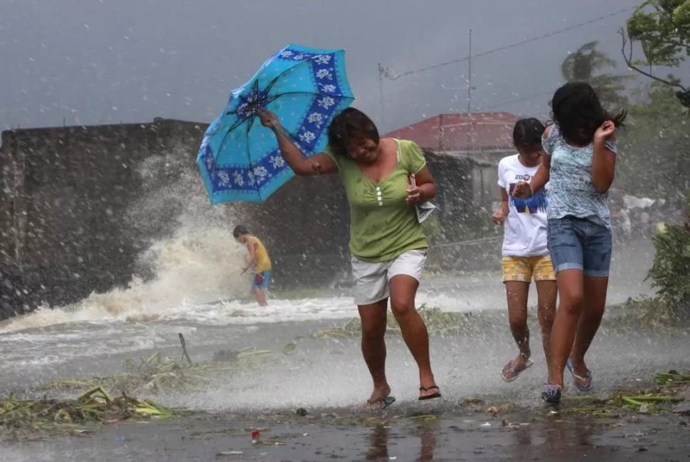 AL SUR DE MANILA. Residentes de la capital de Filipinas buscan ponerse a resguardo del viento que provoca un gran oleaje sobre la costa. REUTERS