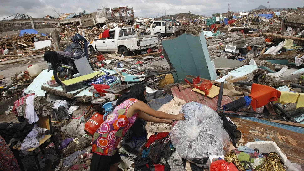 DEVASTACIÓN. Una mujer seca sus ropas en medio de las pilas de escombros que dejó el paso de Haiyan. REUTERS