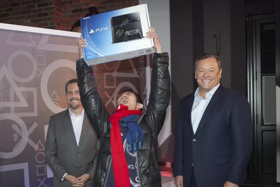 FELIZ. Un joven neoyorkino levanta la caja de la consola que consiguió; a su izquierda, Tretton, CEO de Sony. REUTERS