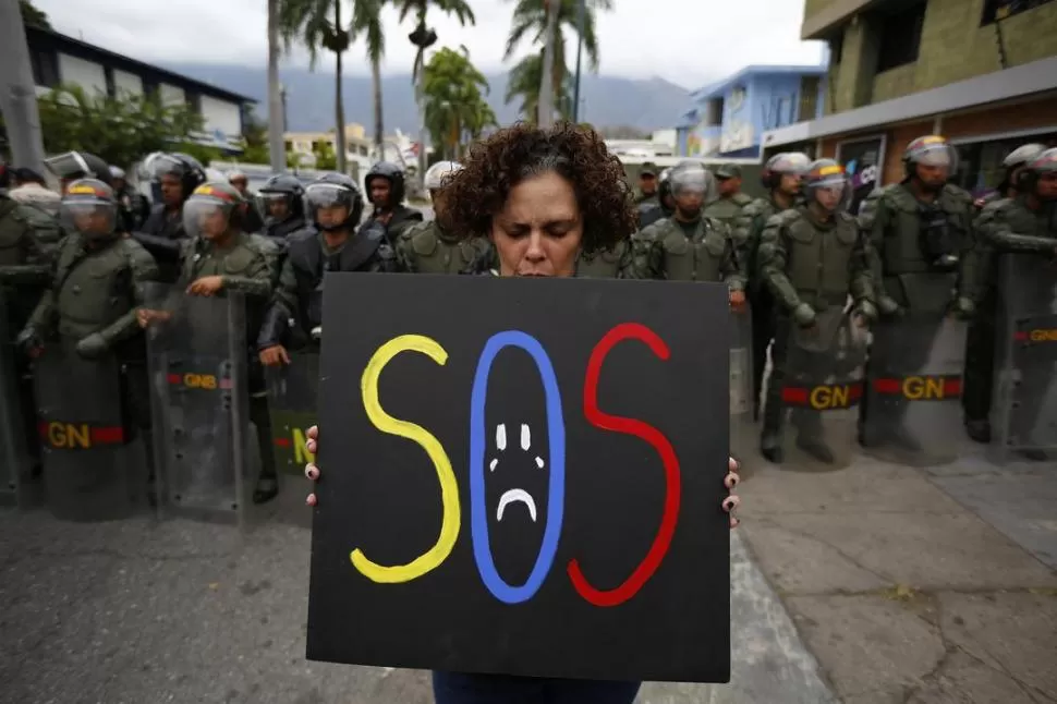 FRENTE A LA EMBAJADA DE CUBA. Una militante de la oposición sostiene esta elocuente pancarta, ante una formación de la policía militarizada. reuters 