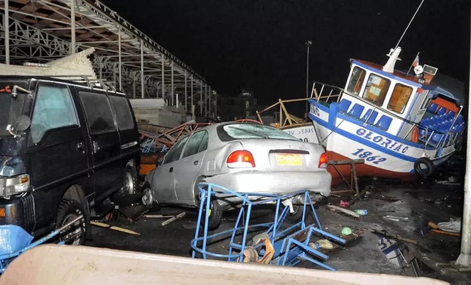 DAÑOS. La fuerza de las olas y el movimiento sísmico terminaron apiñando vehículos y un barco pesquero en la orilla del mar, en el puerto de Iquique.  