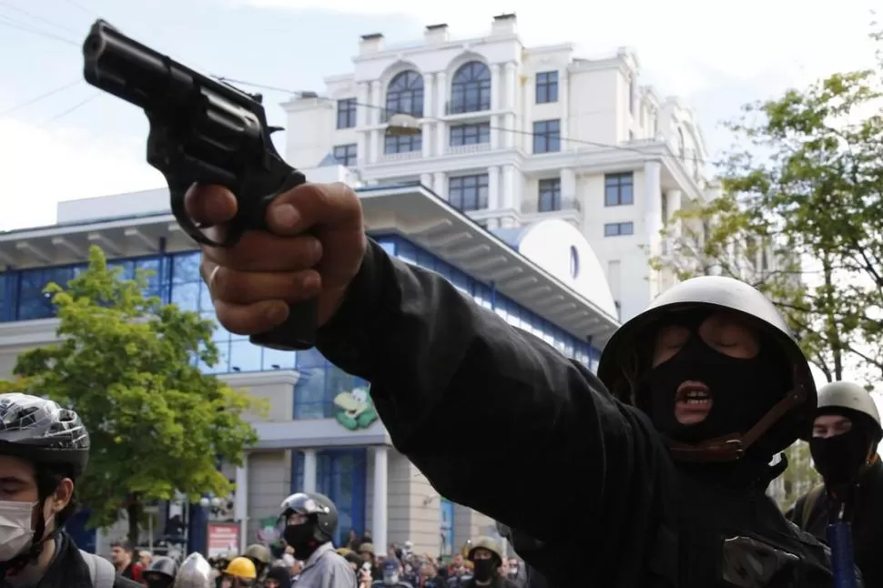LUCHA. Un activista prorruso amenaza con una pistola a los partidarios del Gobierno de Ucrania, durante el enfrentamiento callejero previo a al incendio de la sede sindical, en Odessa. REUTERS