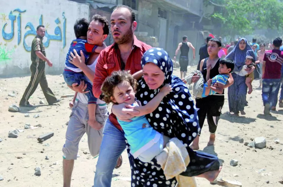 UN ATAQUE. Palestinos huyen con sus hijos en brazos de las bombas israelíes, en la ciudad de Gaza. reuters