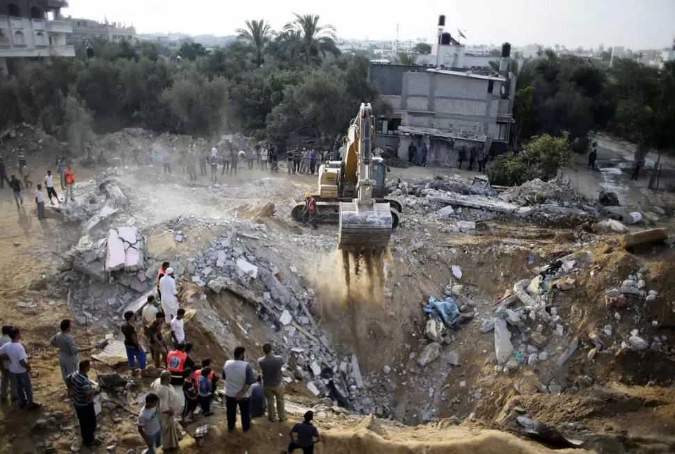 LOS ATAQUES. En Khan Younis, una excavadora trabaja en un lugar donde había una casa. En Ashkelon, policías eliminan los restos de un cohetes. fotos reuters