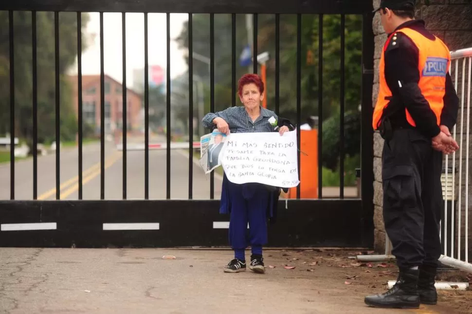 EL PÉSAME DE TODOS. En las puertas del predio un custodio acompaña a una señora que sostiene la cartulina con la foto de Grondona y un mensaje para su familia. 