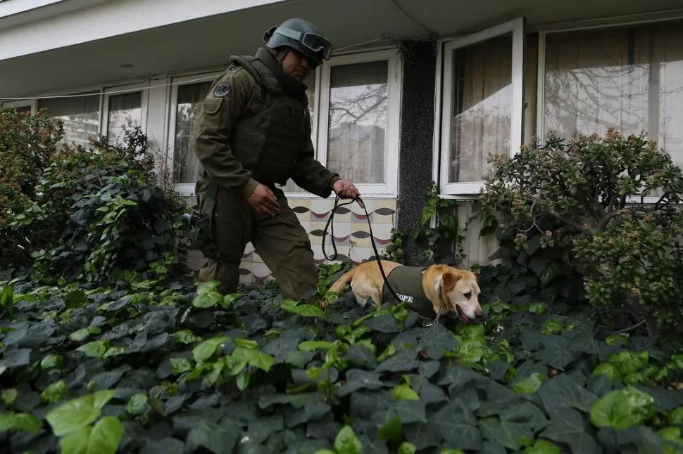 INSPECCIÓN. Un policía chileno, ayudado por un perro, busca indicios que ayuden a esclarecer el atentado. REUTERS