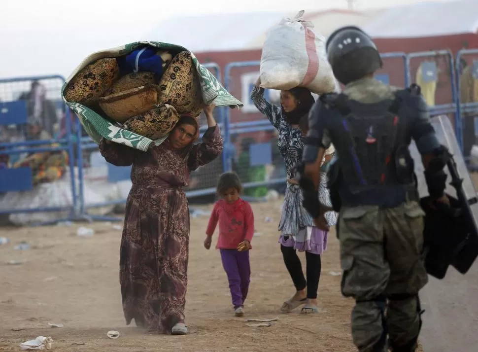 EN SUELO TURCO. Mujeres kurdas de Siria llevan las pocas pertenencias que pudieron retirar de sus casas. Los guardias turcos abrieron la frontera. reuters