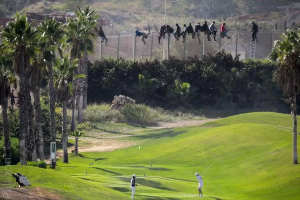 CONTRASTES. Aunque los inmigrantes parecen dispuestos a saltar la valla, los jugadores de golf no se muestran dispuestos a suspender el partido que juegan. REUTERS