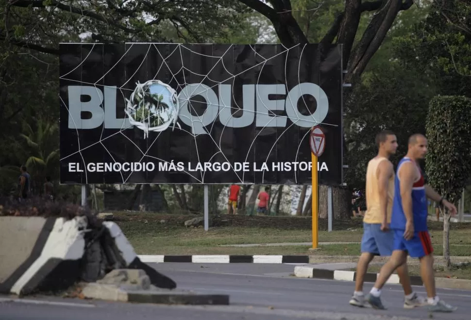 EN LA HABANA. Gimnastas cubanos caminan frente un cartel que advierte sobre el bloqueo que sufre la isla. reuters