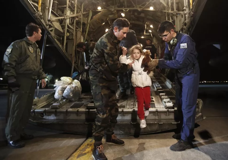 EN ATENAS. Pilotos griegos de un C-130 que trasladó a pasajeros del ferry, ayudan a descender a una niña del avión. reuters