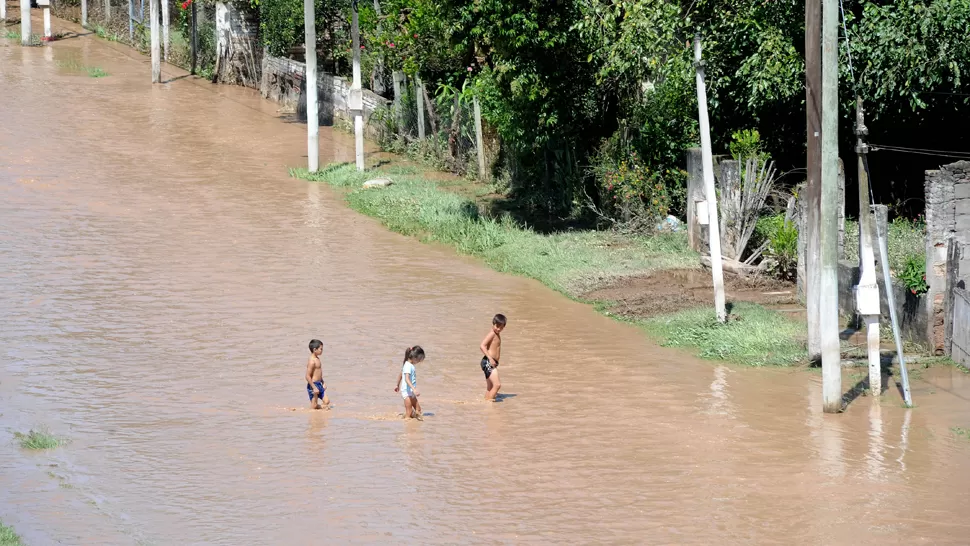 TRISTE POSTAL. Tres niños avanzan por un camino cubierto de agua que desbordó del río Lules. LA GACETA / FOTO DE HÉCTOR PERALTA