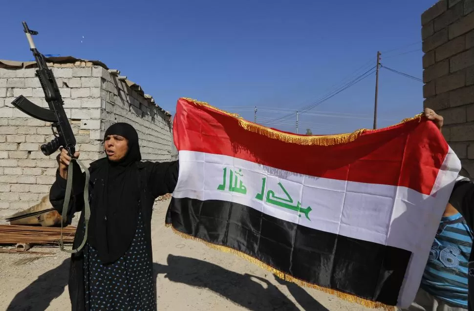 CERCA DE TIKRIT. Una mujer con un Kalasnikov y sujetando una bandera iraquí saludan a las tropas. reuters