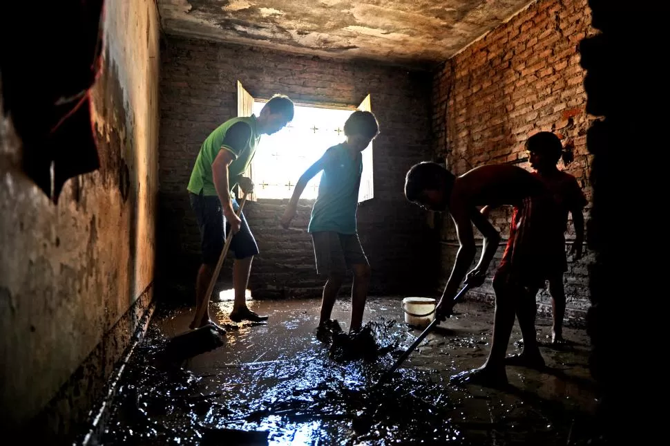 TAREA ARDUA. Cuatro chicos intentan sacar el barro que se metió en su casa tras las últimas inundaciones. la gaceta / foto de franco vera