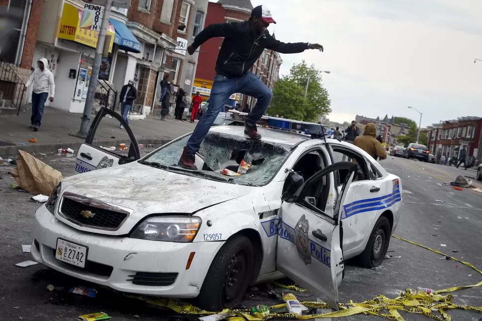 CAOS. Uno de los manifestantes destruye un auto policial, en Baltimore. reuters