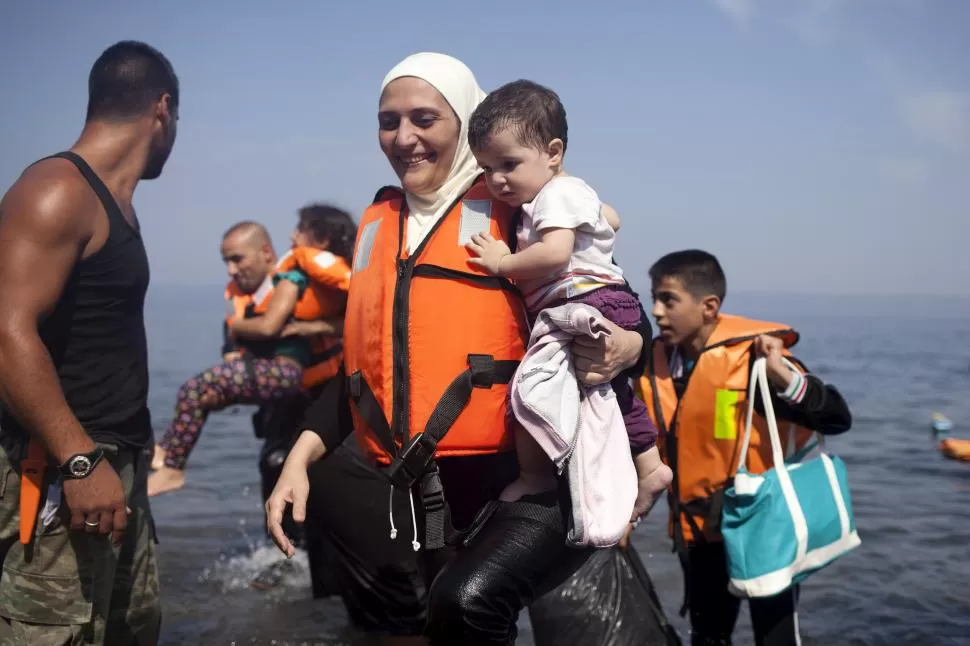 A SALVO. Una mujer siria, cargando a su hijo, sonríe aliviada, al descender de una balsa que la llevó a la isla griega de Lesbos. reuters