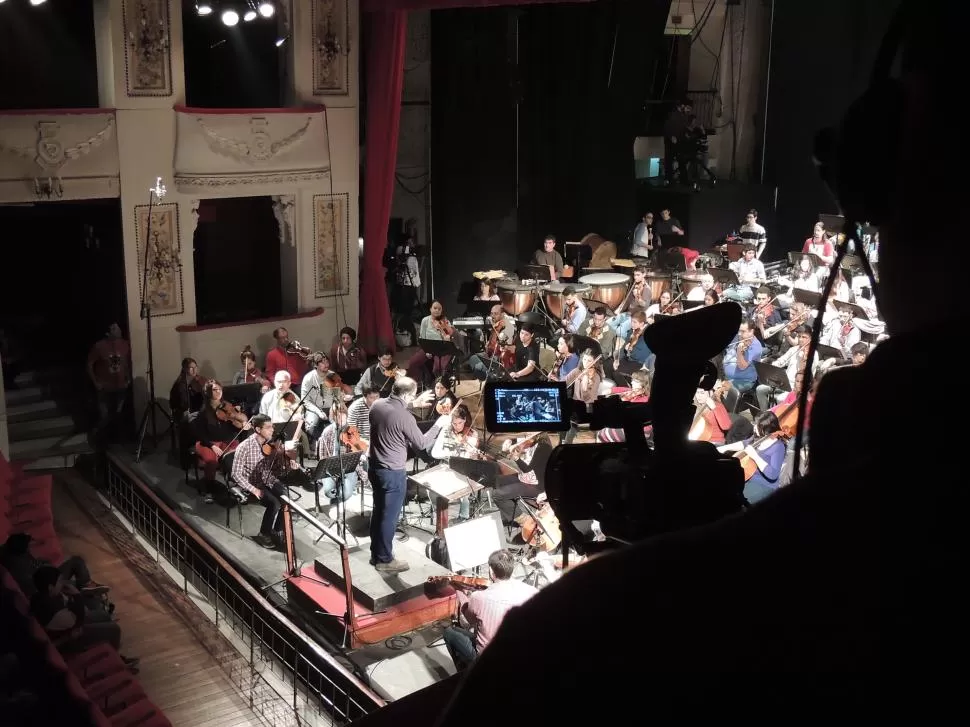 EN ENSAYO. Gustavo Guersman dirige a los músicos juveniles, mientras son filmados desde uno de los palcos del primer piso del teatro Alberdi. Fotos gentileza dirsav