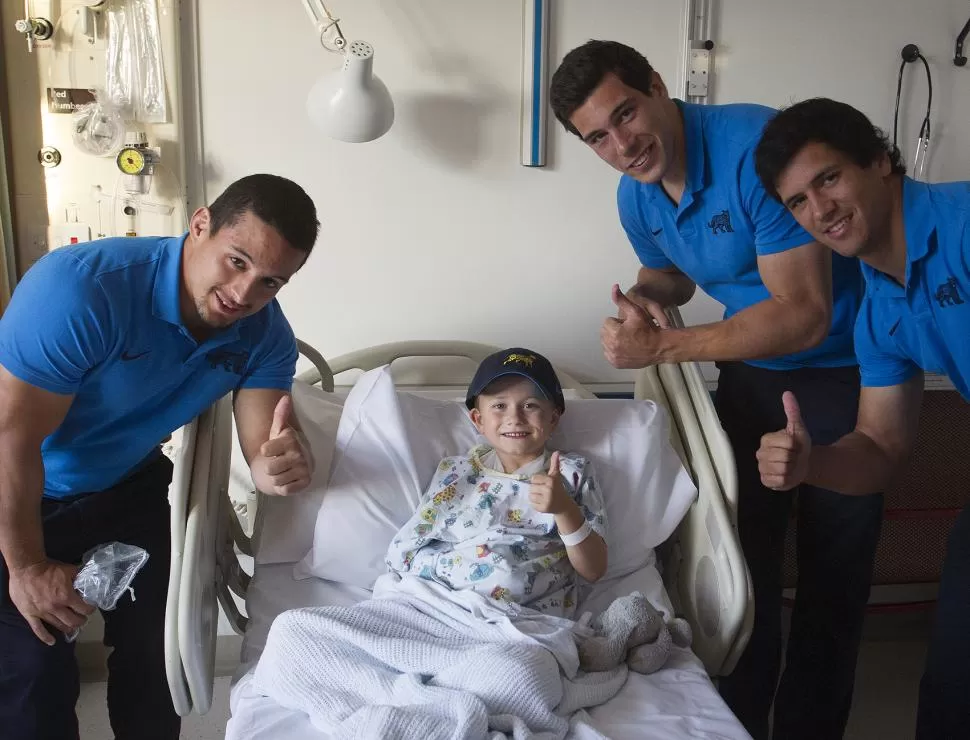 SOLIDARIDAD. Juan Pablo Socino, Guido Petti y Matías Moroni saludan junto a un niño enfermo de cáncer, durante su visita al Royal Hospital de Gloucester. El rugby no se termina en la cancha. PRENSA UAR