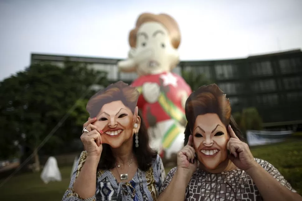 BURLA. Mujeres con máscaras con la imagen de Rousseff protestan en Brasilia. reuters 