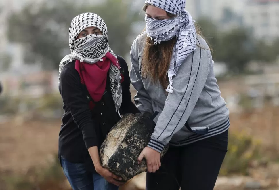 CERCA DE RAMALAH. Dos chicas palestinas llevan una piedra para armar una barricada contra la policía israelí. REUTERS
