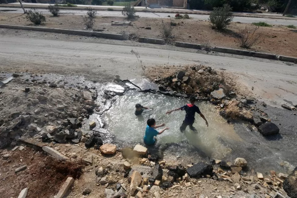 VIVIR EN LAS RUINAS. Niños de Alepo juegan en un pozo con agua de una tubería dañada por bombardeos. Reuters