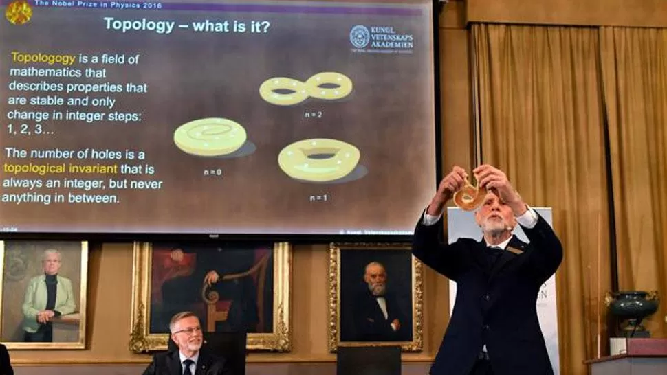 SENCILLO. Thomas Hans Hansson, miembro de la Academia de Ciencias Sueca, explica qué es la topología con un pretzel al anunciar el Nobel de Física. REUTERS