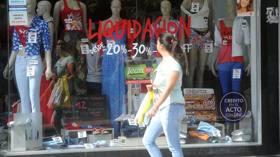 COMERCIOS. Una mujer pasa frente a una vidriera tucumana plagada de liquidaciones y ofertas; los comerciantes aseguran que no logran repuntar las ventas. ARCHIVO