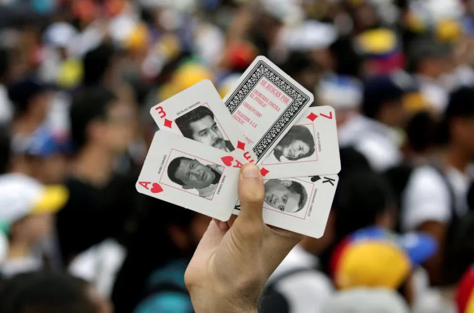 LOS CUATRO. Un opositor muestra un juego de cartas con el rostro de los que define como responsables de la crisis. reuters 