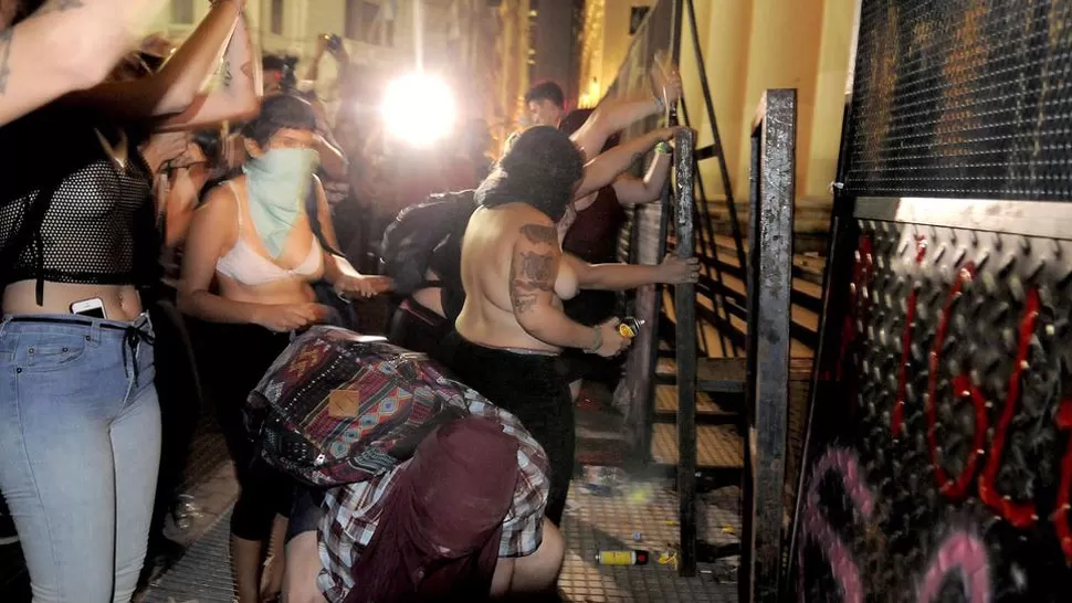 CON LOS ROSTROS CUBIERTOS. Las mujeres intentan derribar las vallas que protegen la Catedral porteña. FOTO TOMADA DE INFOBAE.COM