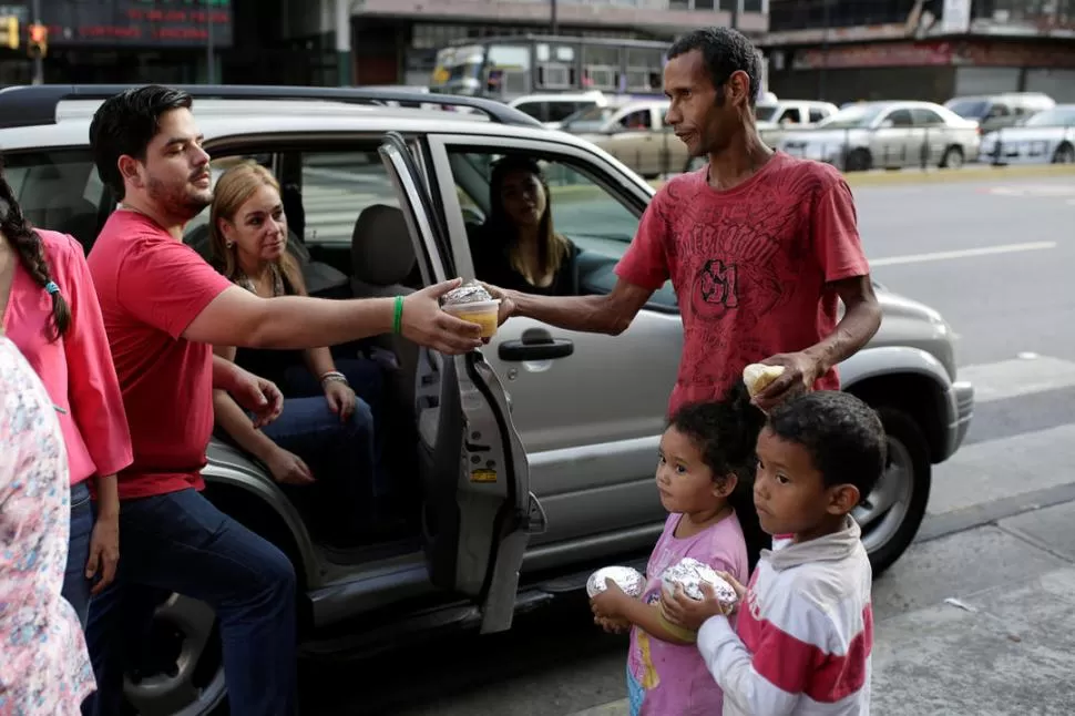 CARIDAD. Diego Prada da una taza de sopa a un hombre en Caracas.  reuters 