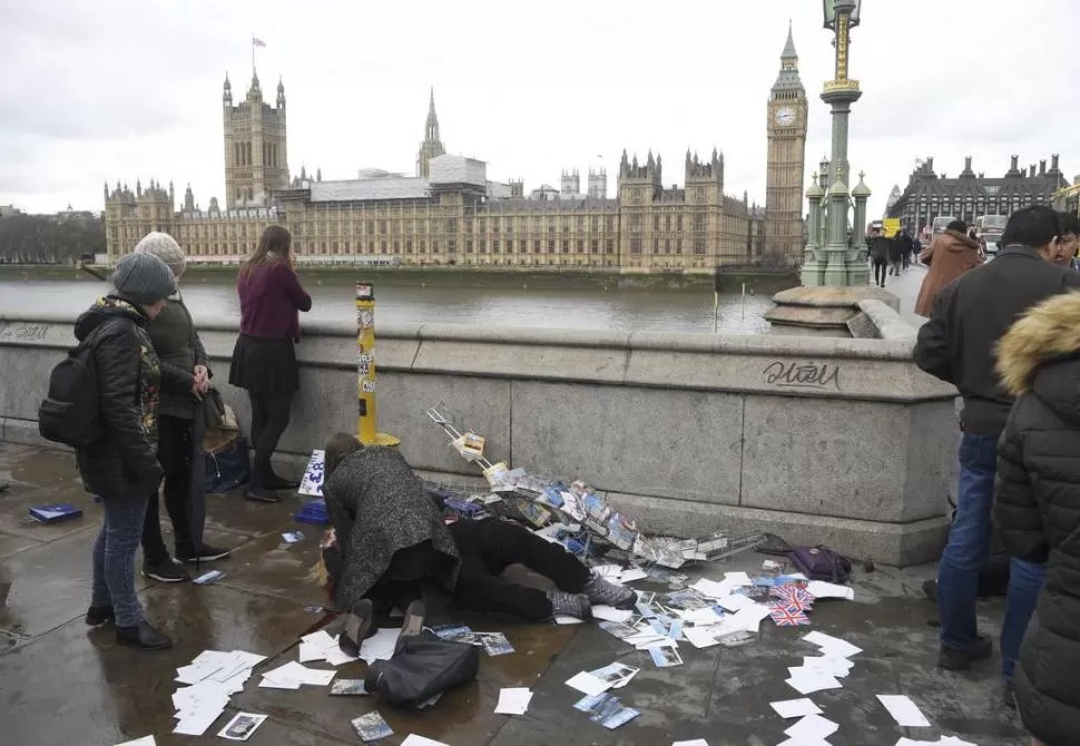 PERPLEJIDAD Y SOLIDARIDAD. Una transeúnte brindó las primeras atenciones a una de las víctimas, en uno de los accesos al puente de Westminster. fotos reuters 