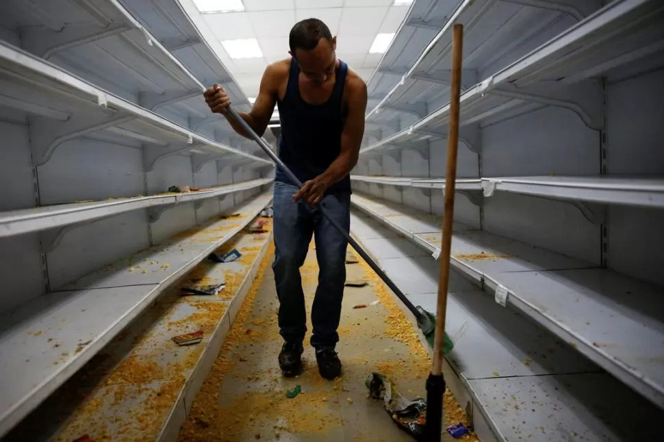 HAMBRE. Un trabajador limpia las estanterías en un mercado después de haber sido saqueado en Caracas. fotos de reuters