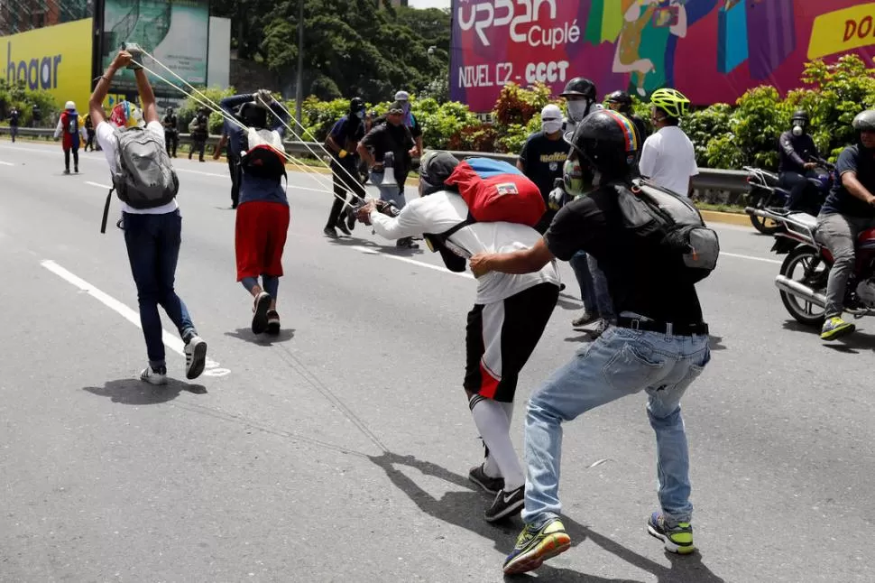 HONDA GIGANTE. Cuatro manifestantes se preparan para lanzar un elemento contundente contra los policías. reuters