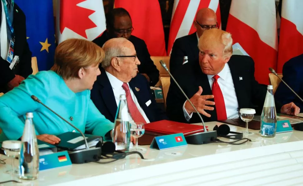 GESTOS DUROS. Merkel y Trump dialogan por delante del presidente de Túnez, Beji Caid Essebsi, antes del plenario del G7 que se celebró en Taormina. reuters