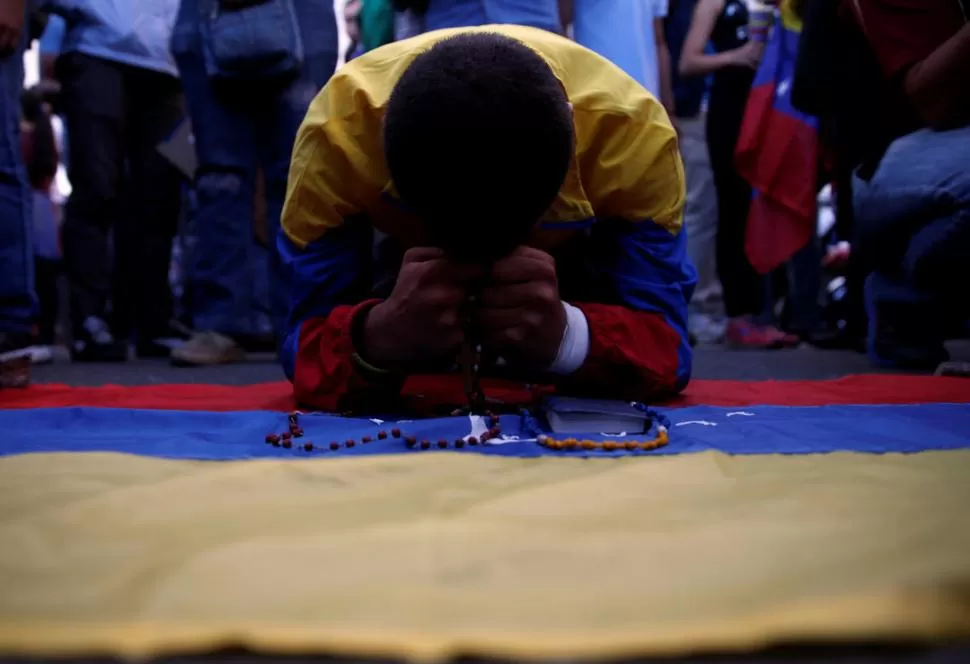 ORACIONES Y RECLAMOS. Un manifestante reza durante la vigilia para homenajear a los muertos durante las protestas en Caracas.  fotos reuters