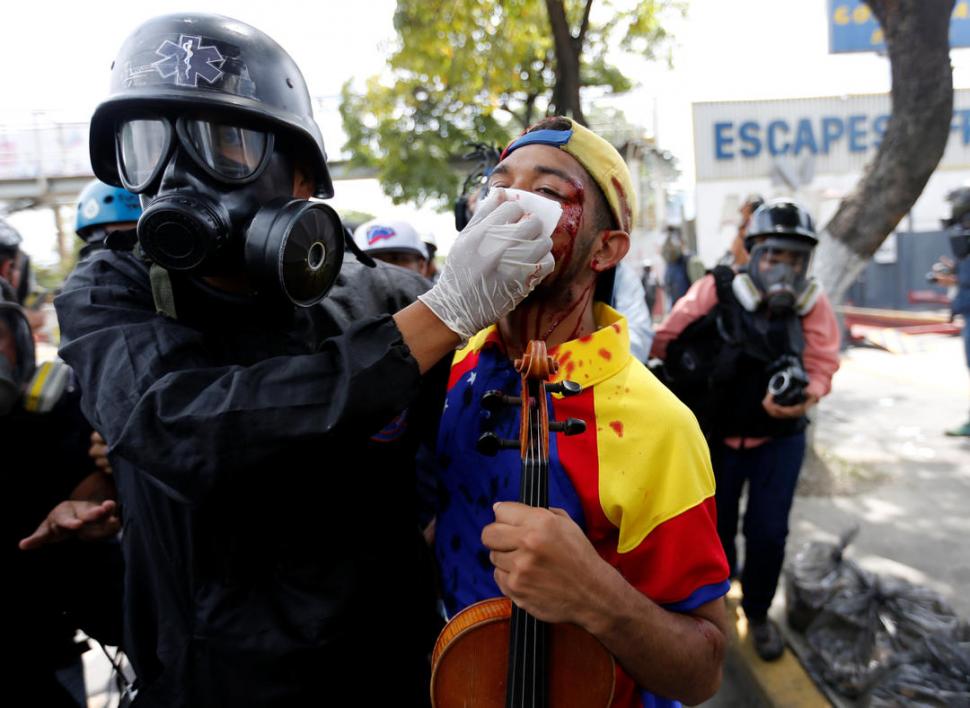 ASISTENCIA. Un enfermero limpia las heridas en el rostro de Arteaga, que lleva el violín a todas las manifestaciones. Reuters